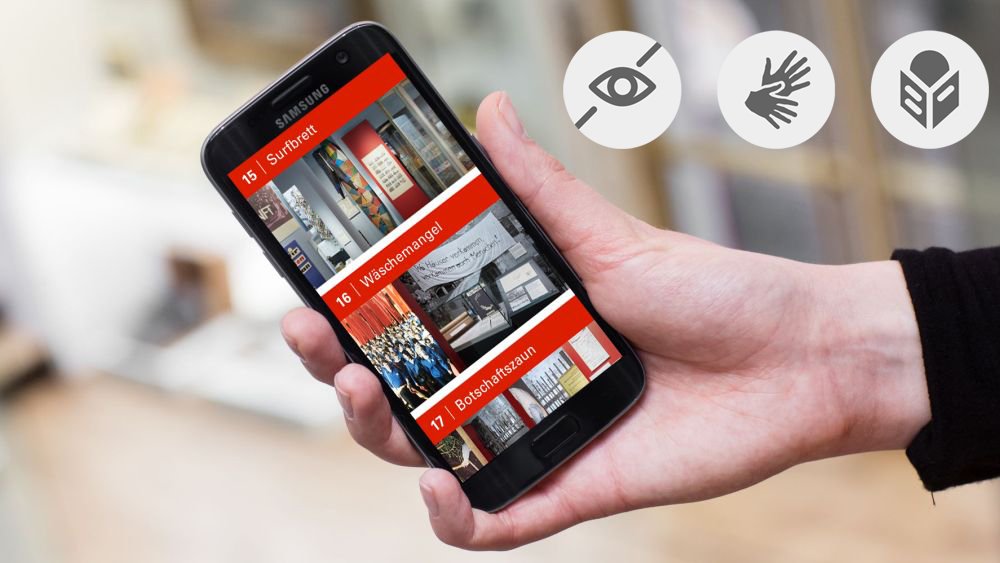 Eine Hand hält ein Smartphone mit dem AudioGuide zur Dauerausstellung auf dem Display.