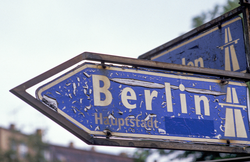 Blaues Verkehrsschild, das den Weg zur Hauptstadt Berlin angibt und nach links zeigt.