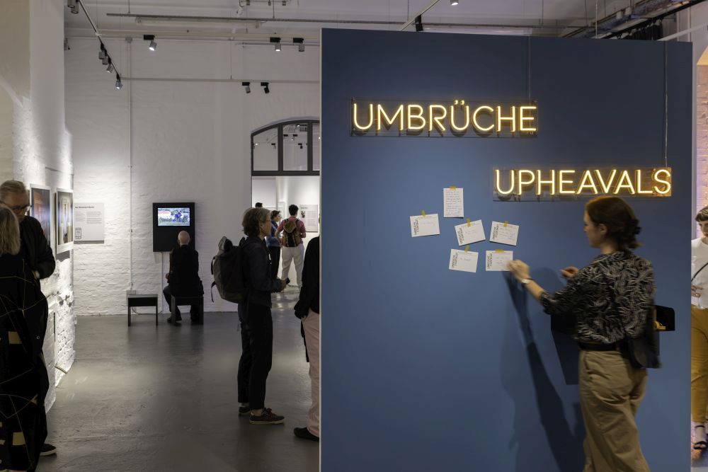 Besucherin vor einer Pinnwand mit dem Schriftzug "Umbrüche. Upheavals" in der Ausstellung.