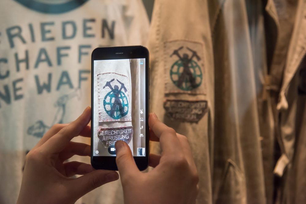 Two hands are holding a smartphone to take a picture of the self-made clothes of the peace movement