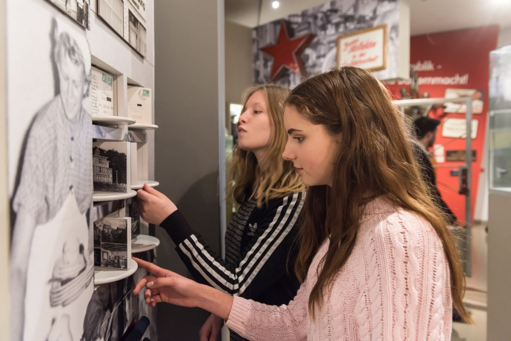 Zwei Mädchen im Teenager-Alter schauen sich an einer Wand in der Ausstellung Elemente mit Fotos zum Drehen an