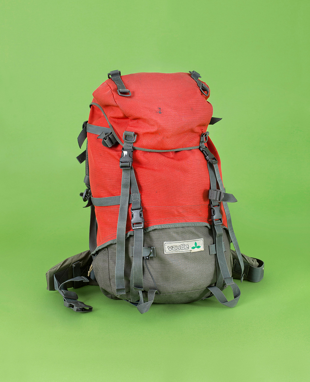 VauDe hiking backpack. Red-grey, worn. On a green background.