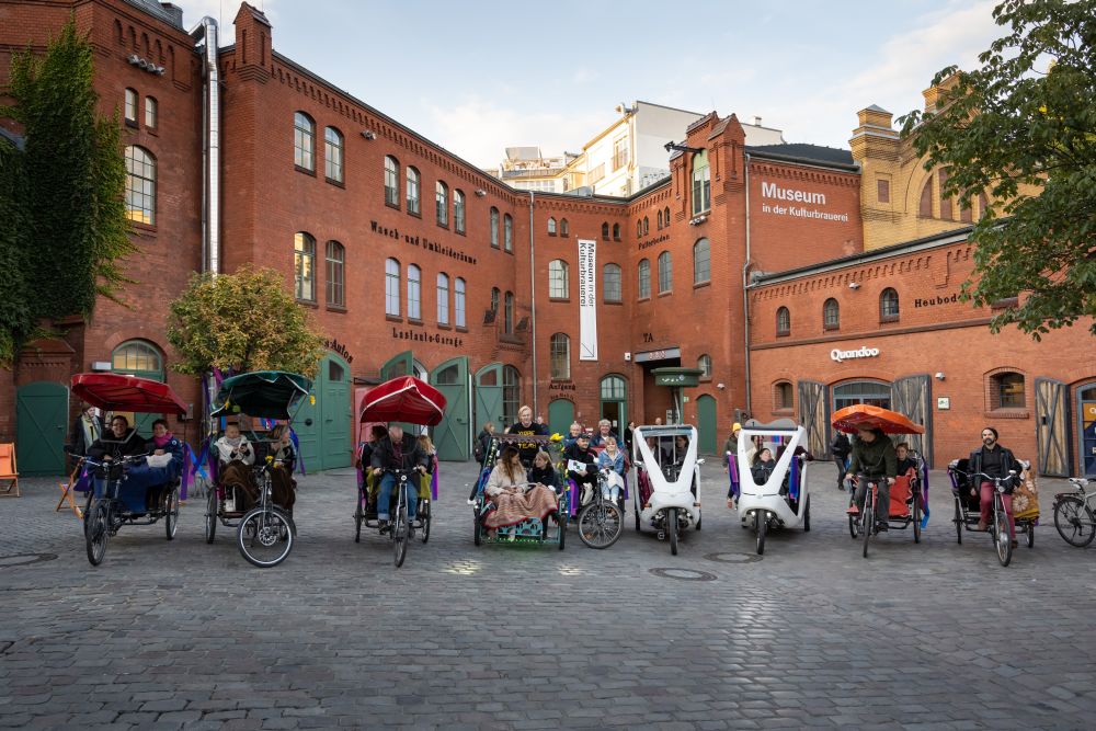 Personen in Fahrrad-Rikschahs vor dem roten Backsteingebäude Museum in der Kulturbrauerei.