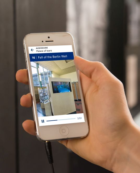 Hand with smartphone, on the display you can see the AudioGuide for the permanent exhibition 'Site of German Division' in the Tränenpalast