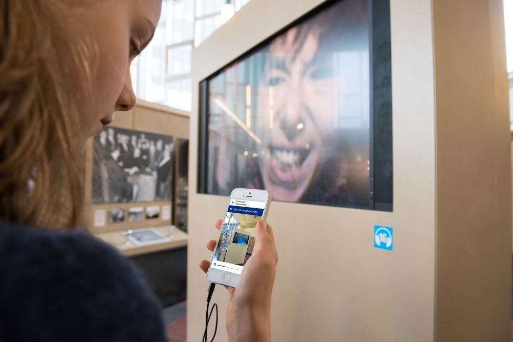 Hand with smartphone, on the display you can see the Audioguide for the permanent exhibition 'Site of German Division' in the Tränenpalast