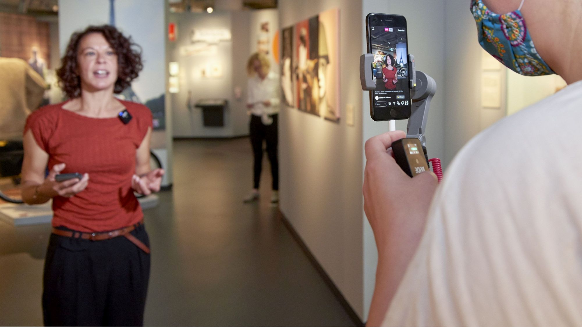 Eine Frau wird in einem Ausstellungsraum mit einem Smartphone gefilmt.