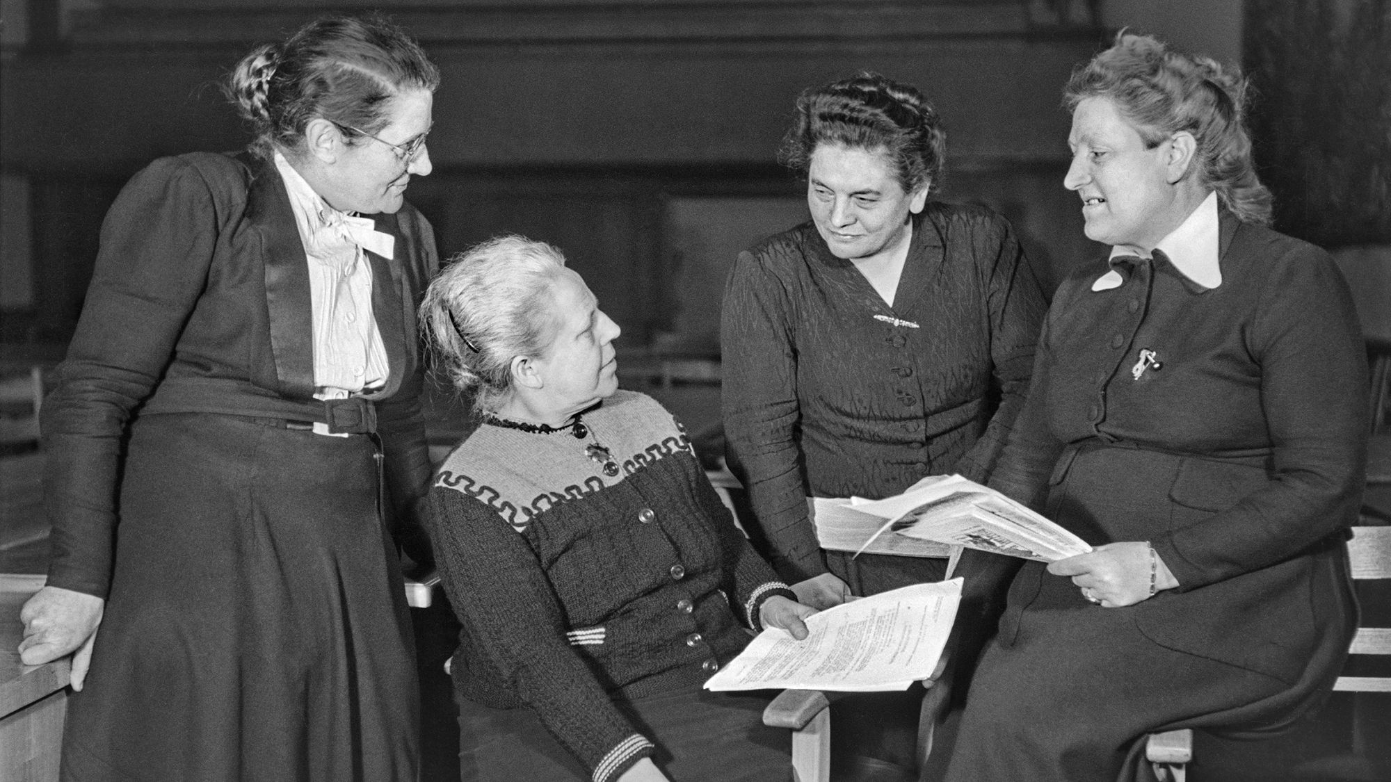 Auf dem historischen Foto sitzen Helene Wessel, Helene Weber, Friederike Nadig und Elisabeth Selbert nebeneinander und schauen sich gegenseitig an.