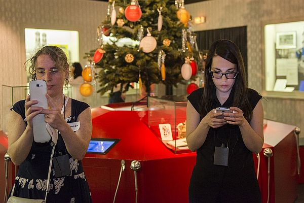 Zwei Frauen stehen vor einem ausgestellten Weihnachtsbaum und tippen in ihre Smartphones