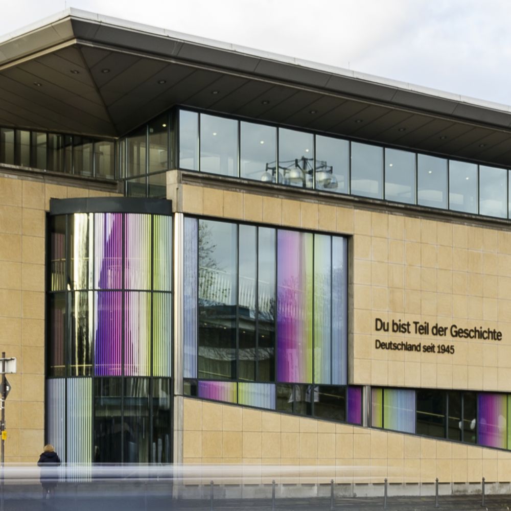 Außenansicht des Hauses der Geschichte in Bonn mit Sandstein, viel Glas, bunten Grafiken und dem Schriftzug "Du bist Teil der Geschichte"..