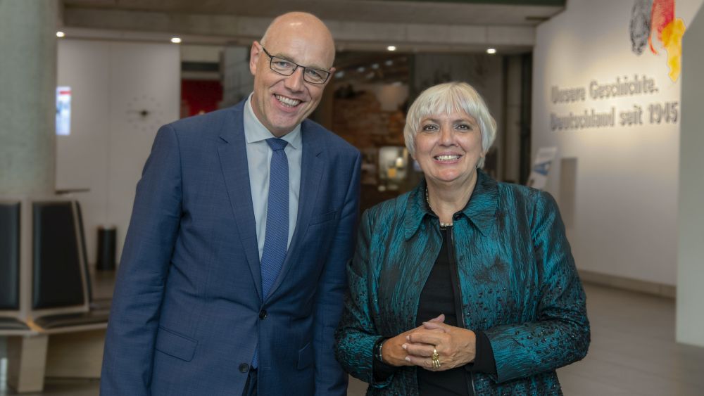 Harald Biermann und Claudia Roth stehen nebeneinander im Haus der Geschichte.