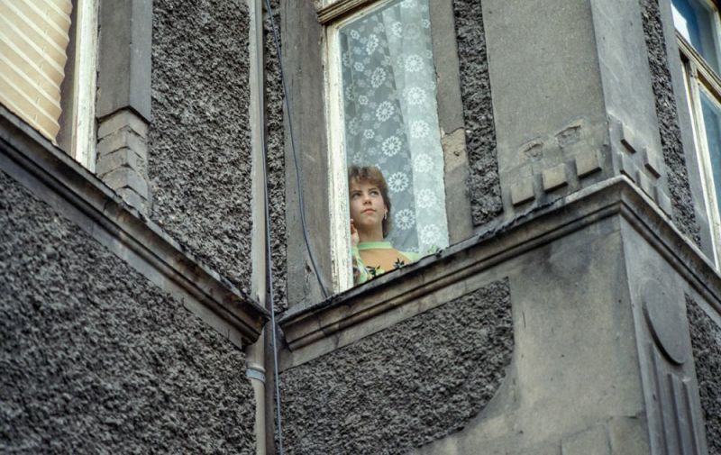 Eine junge Frau blickt aus dem Fenster eines grauen Hauses 