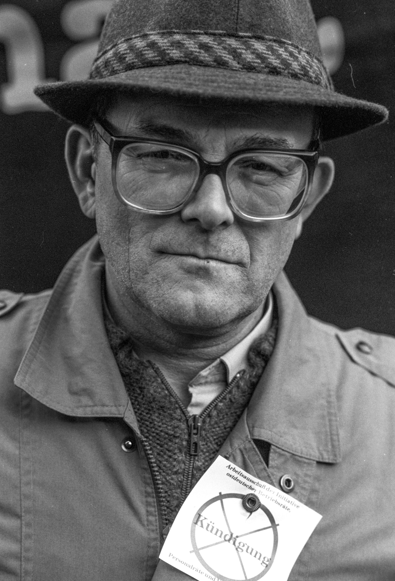 Ein mittelalter Mann mit Hut und Brille und einem Anstecker mit dem durchgestrichenen Wort Kündigung.