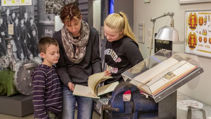 Foto: Eine Frau zeigt zwei Kindern ein Buch in der Ausstellung.