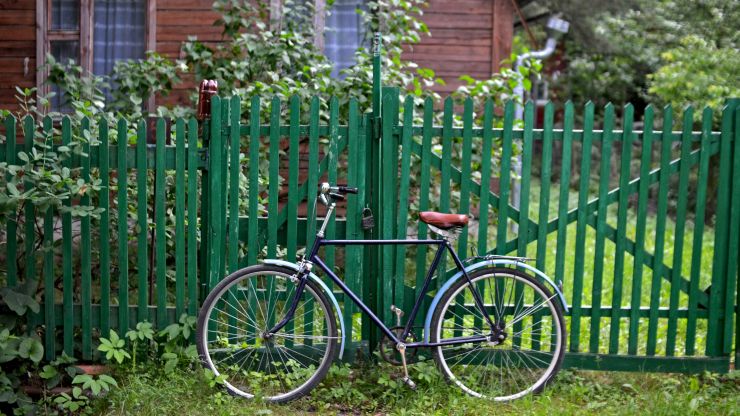 Fahrrad lehnt an grünem Zaun vor Holzhütte im Grünen