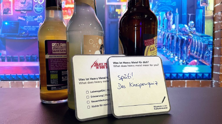Bierdeckel mit Quizfragen und Aufschrift "späti!- das Kneipenquiz" an Flaschen angelehnt