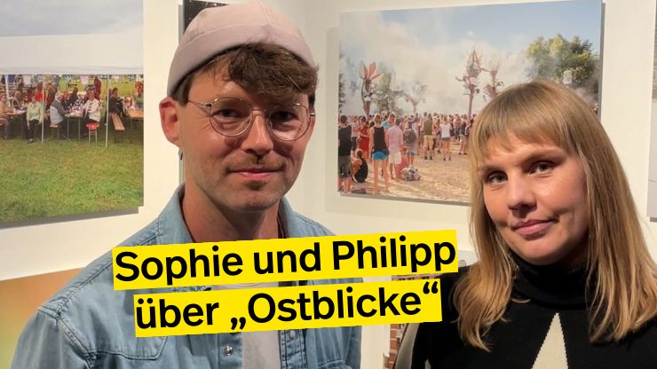 Porträtfoto von Sophie Kirchner und Philipp Baumgarten vor Fotografien in der Ausstellung  „Ostblicke“