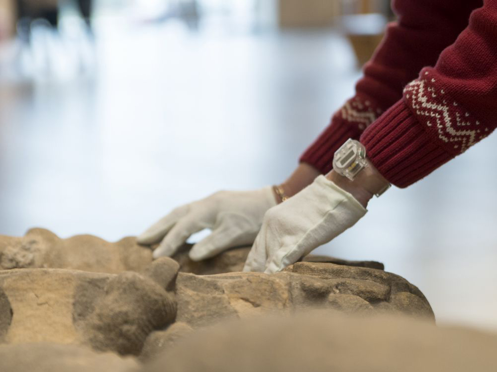 Hände tasten ein Museums-Objekt aus Stein