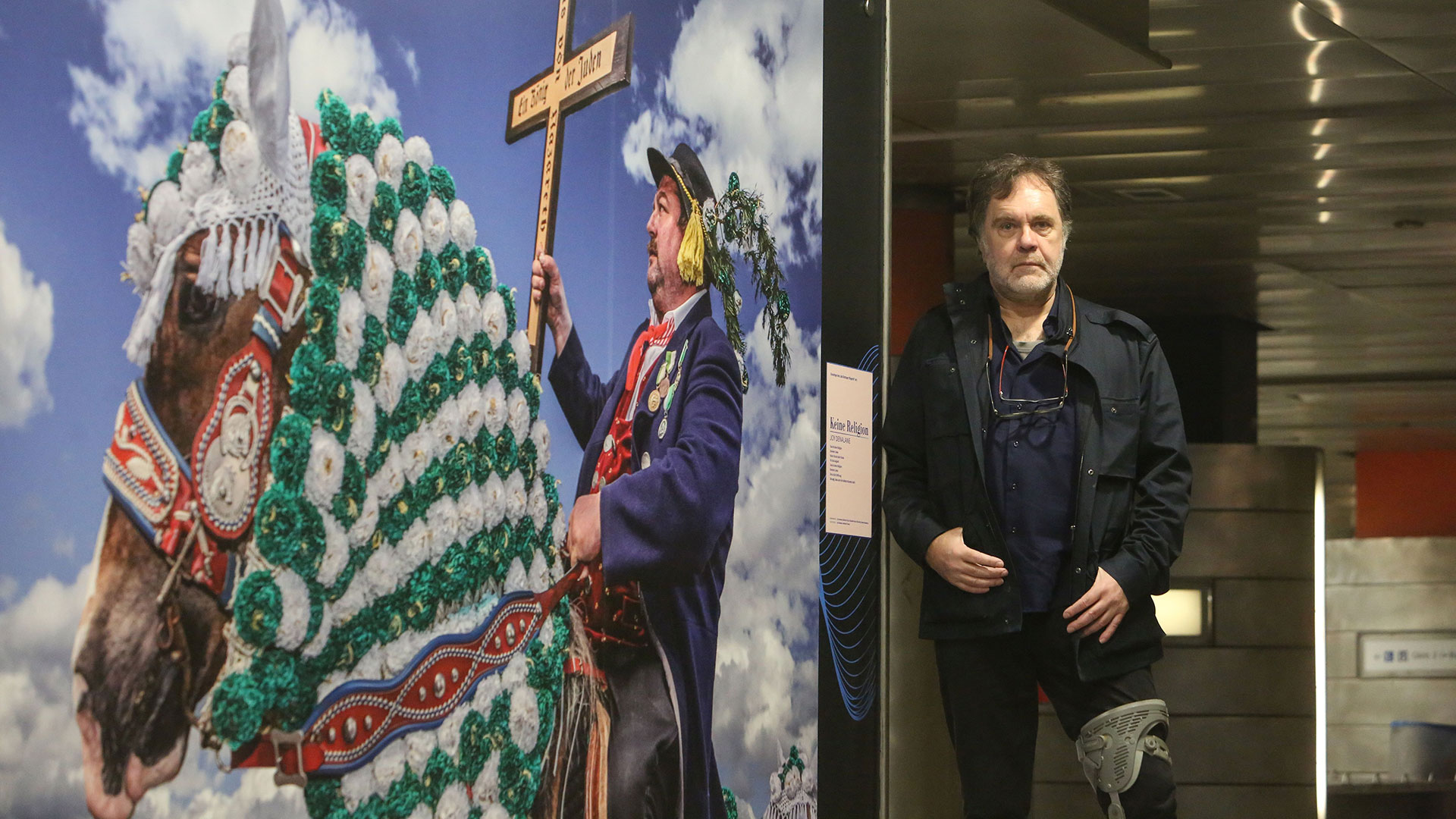 Hans-Jürgen Burkard vor seinem Foto Im linken Teil des Bildes sieht man eine Fotografie von Hans-Jürgen Burkard, das ein Kaltblut mit Tracht zeigt. Rechts steht der Fotograf.