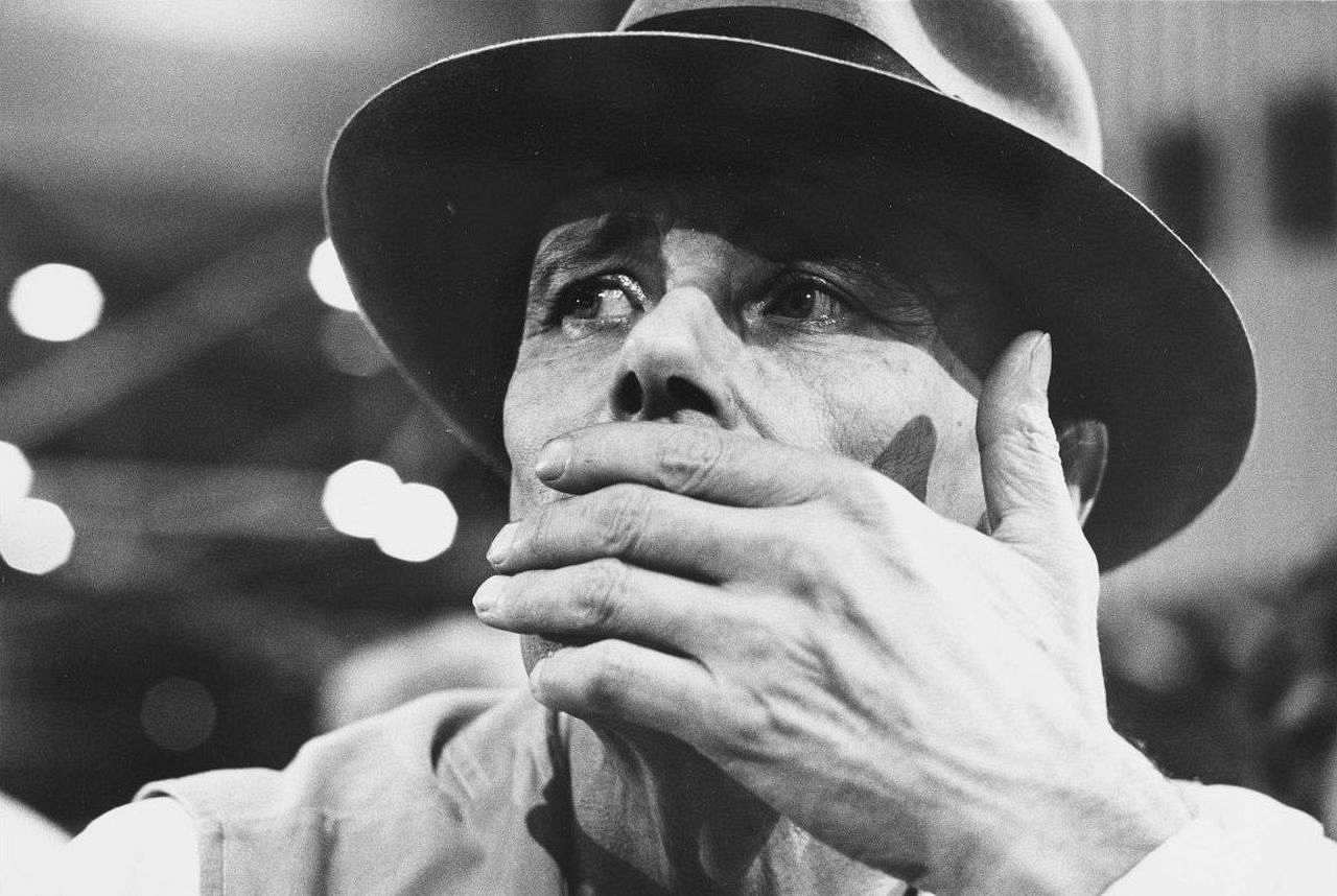 Porträtfoto des Aktionskünstlers Joseph Beuys, der seinen bekannten Hut trägt und die linke Hand vor den Mund hält, 1975-1985.