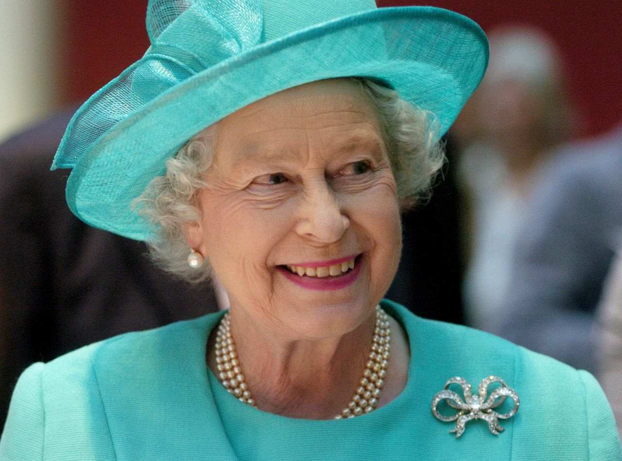 Königin Elisabeth II. lächelt in einem mintgrünen Blazer mit passendem Hut.
