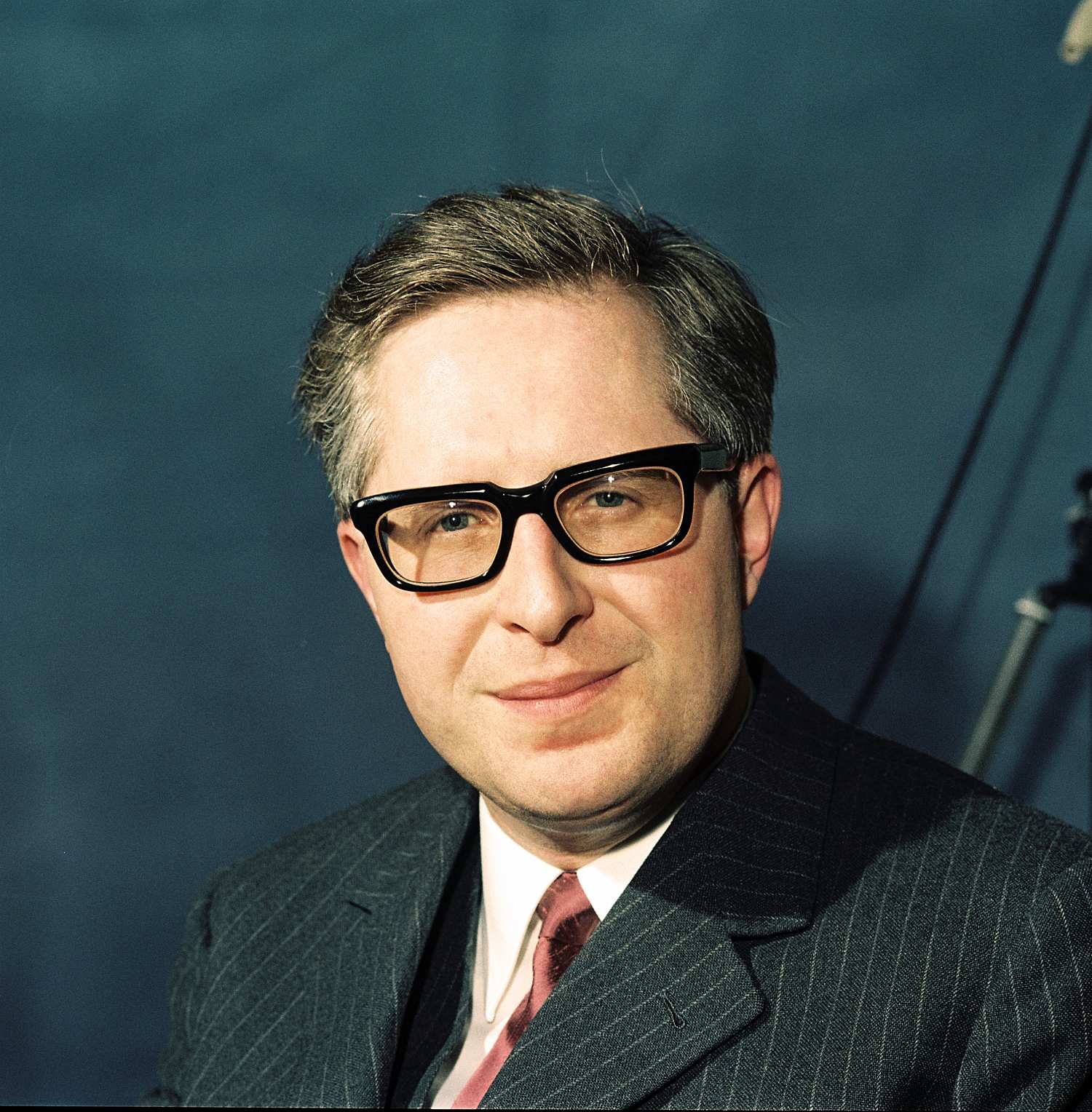 Porträtfotografie des CDU-Politikers Bernhard Vogel, 1970. Er trägt eine schwarze Hornbrille, einen Nadelstreifenanzug mit roter Krawatte und weißem Hemd und lächelt leicht.