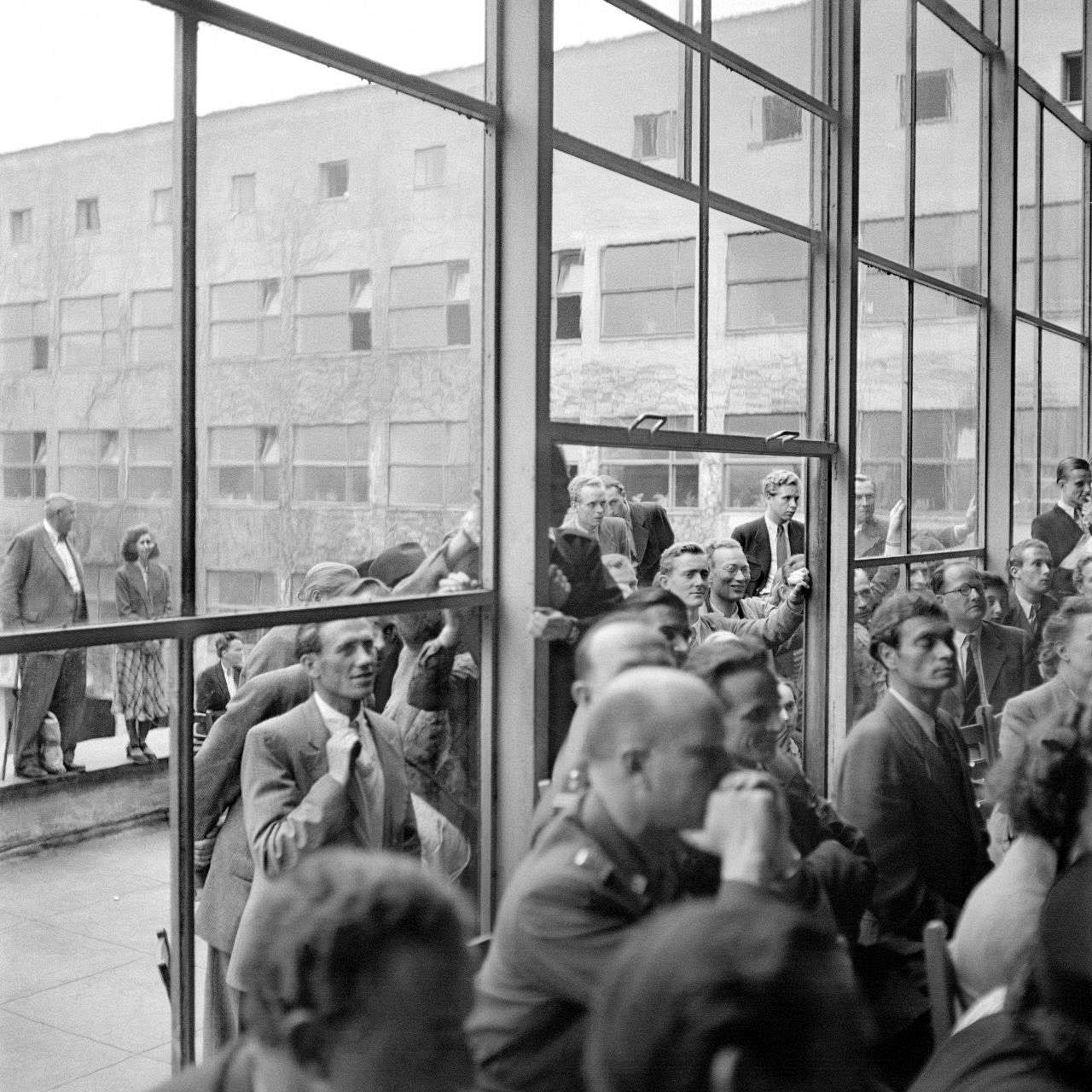 Am 23. Mai 1949 wird das Grundgesetz für die Bunderepublik Deutschland unterzeichnet, bevor es am 24. Mai in Kraft tritt. Erna Wagner-Hehmke ist mit ihrer Kamera vor Ort. Vor der ehemaligen Aula der Pädagogischen Akademie in Bonn, drängen sich Schaulustige, so genannte Zaungäste, die diesen historischen Moment miterleben wollen. Wagner-Hehmke soll die Arbeit des Parlamentarischen Rates fotografisch begleiten. Für ihren Auftrag nimmt sie oftmals ungewöhnliche Perspektiven ein: Sie fotografiert nicht nur während der langen Sitzungen, sondern auch Empfänge, Pausen und die Arbeit hinter den Kulissen. 