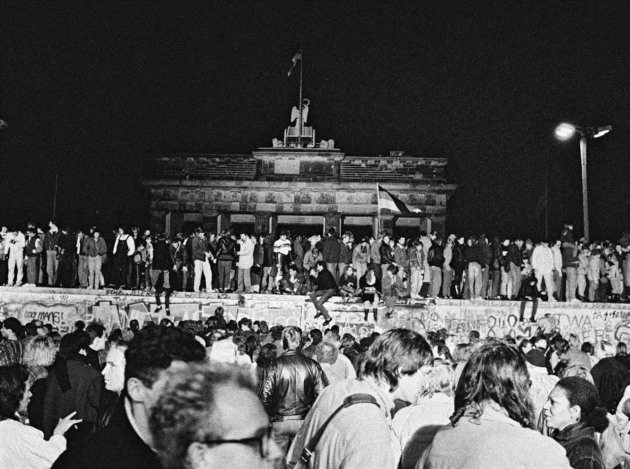 Fotos von feiernden Menschen auf und vor der Berliner Mauer bei Nacht. Zentral im Bild ist das Brandenburger Tor hinter der Mauer zu sehen.