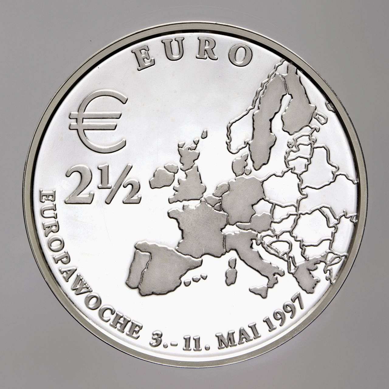 Silberfarben in Kapsel und blauem Originaletui mit Echtheitszertifikat; Vorderseite: Stäbchen, erhabene Umschrift: Europawoche 3.-11. Mai 1997 / Euro; Europakarte, links oben: E 2 1/2; Rückseite: Stäbchen, fünfzackige Sterne, Brandenburger Tor, darunter Berliner Bär.