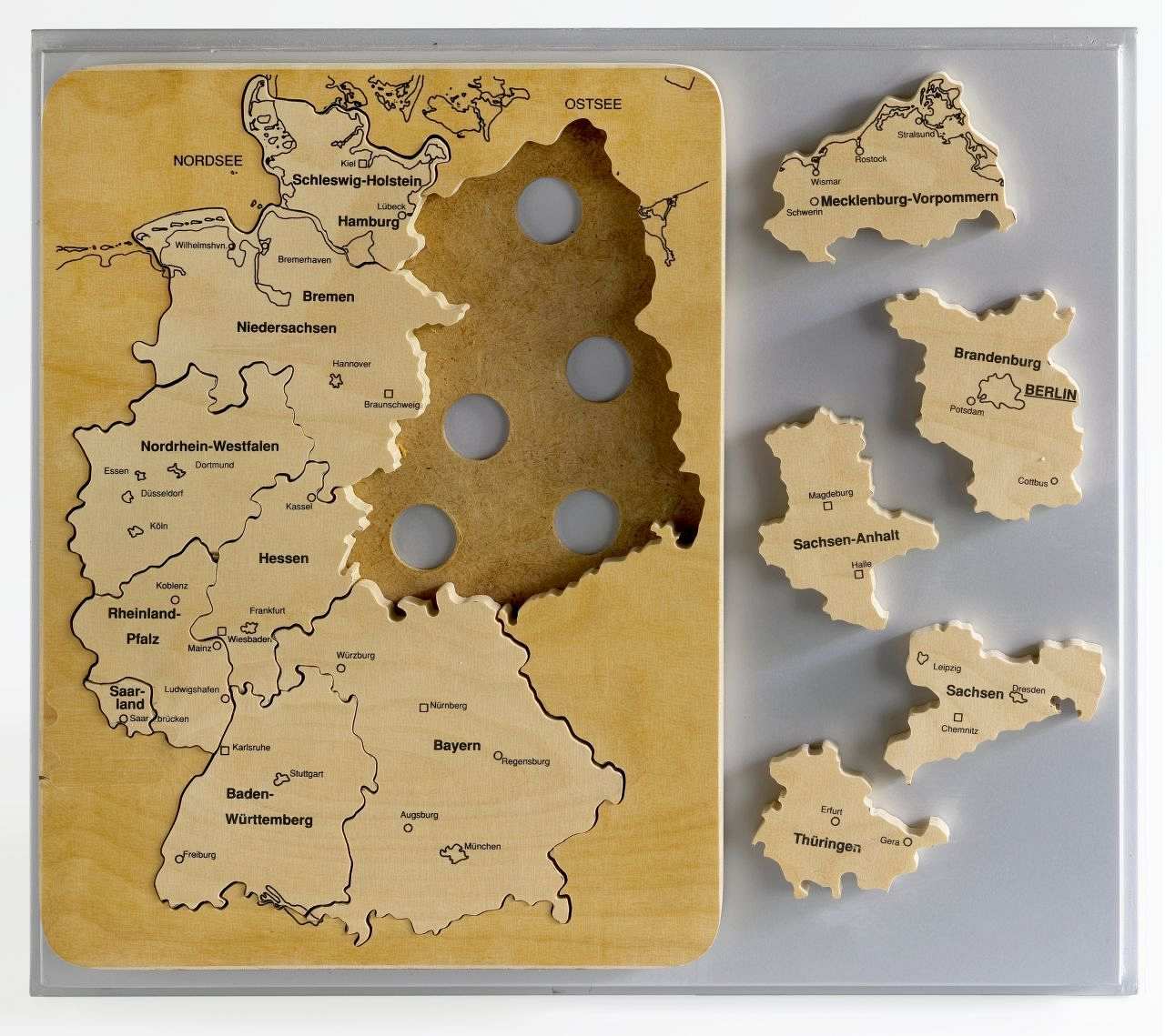 Rechteckige Holzplatte mit abgerundeten Ecken. Darin als Puzzleteile die Umrisse der Bundesländer (einschließlich der fünf neuen). Die wichtigsten Städte sind eingetragen.