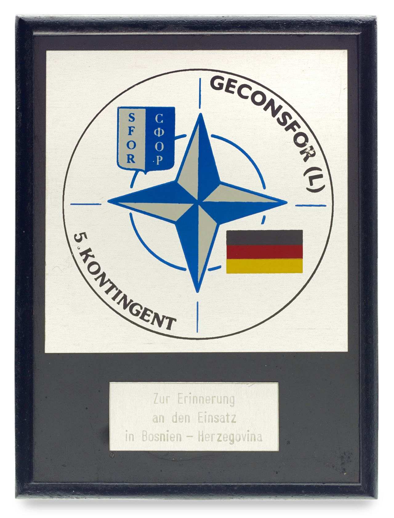 Schwarze Tafel mit aufgelegtem quadratischem Schild. Darauf Abbildung des NATO-Emblems. Oben links SFOR-Wappen, unten rechts deutsche Fahne. Schwarze Umschrift: GECONSFOR (L) 5. Kontingent. Darunter kleine silberfarbene Plakette mit der Inschrift: Zur Erinnerung / an den Einsatz / in Bosnien - Herzegovina. RS weißes Etikett mit folgendem Text: Stab Nationaler Befehlshaber i. E. / Herrn / Oberstleutnant / Udo Beßer / zur Erinnerung an seinen Einsatz / als InftStOffz / beim Stab Nationaler Befehlshaber i.E. / des deutschen Heereskontingentes SFOR / Feldlager Rajlovac, / Juli 1998 / Chef des Stabes / Brandt / Oberst i.G. Mit Unterschrift.