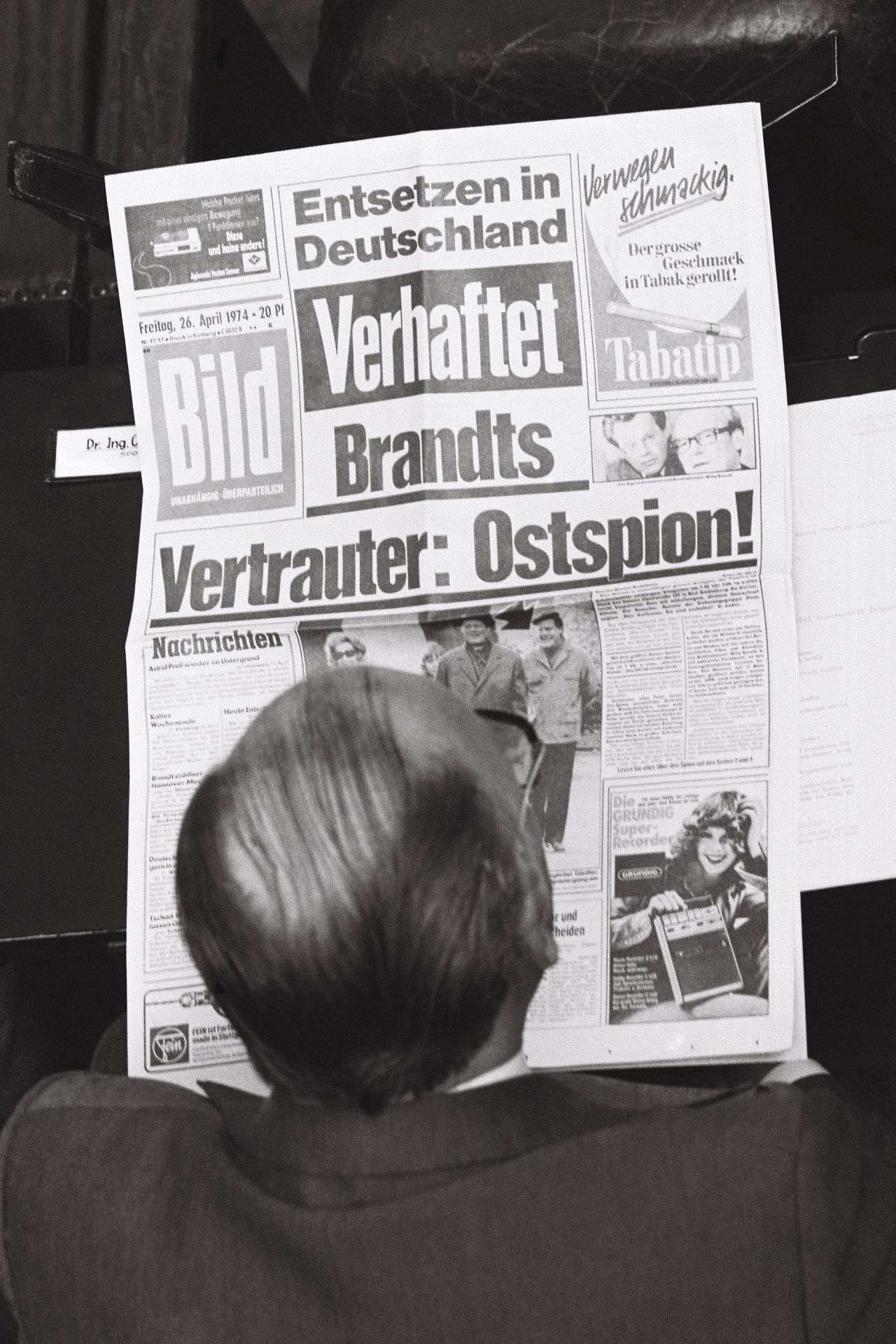 Schwarzweiß-Foto. Kopf und Schulterbereich eines Bundestag-Abgeordneten von oben aufgenommen. Er liest die Bild mit der Titelschlagzeile: ‚Entsetzen in Deutschland, Verhaftet, Brandts Vertrauter: Ostspion!‘.