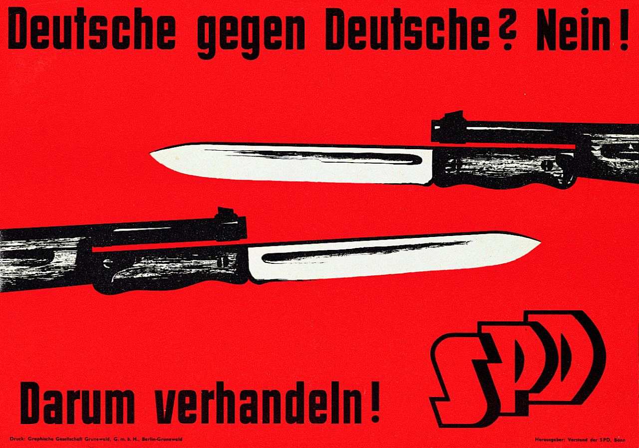 Rotes Plakat mit schwarzer Schrift. Text: Darum verhandeln! SPD. Abbildung von zwei Gewehren mit aufgesetztem Bajonett, die gegeneinander gerichtet sind.