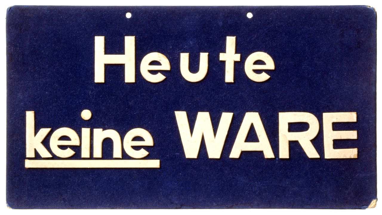 Weiße Schrift (Heute keine Ware) auf blauem Grund. 'Keine' unterstrichen. Oben zwei Löcher zum Aufhängen des Schildes.