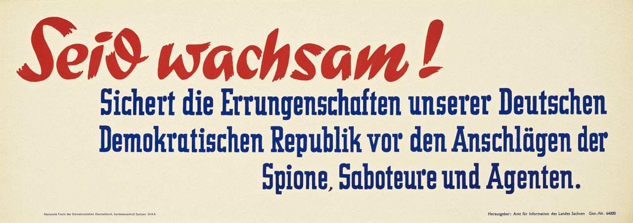 Weißgrundiges Plakat mit rotem und blauem Text: 'Sichert die Errungenschaften unserer Deutschen Demokratischen Republik vor den Anschlägen der Spione, Saboteure und Agenten.' Plakatstreifen.
