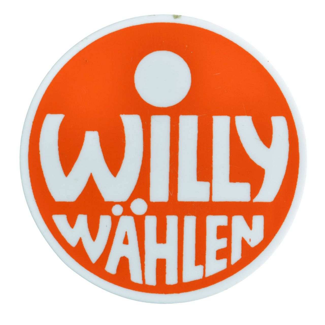 Weißfarbener runder Button mit rotem Kreis und weißer Innenschrift: Willy wählen. Befestigungsnadel auf der Rückseite.