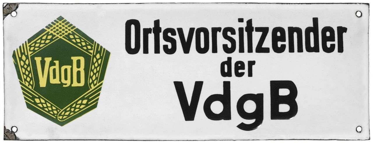 Weißes Schild mit schwarzer Schrift: Ortsvorsitzender der VdgB und links davon das grün-gelbe Emblem des VdgB mit Ähren.