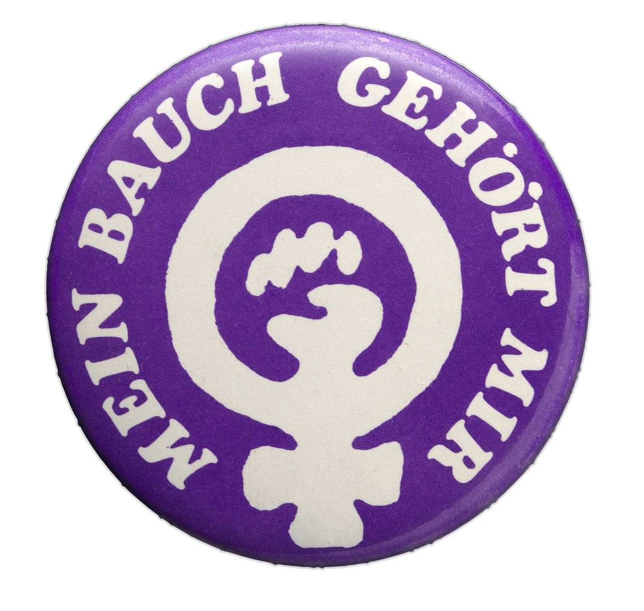 Lilafarbener Button mit weißem Weiblichkeitssymbol. Darin eine Faust. Umschrift: Mein Bauch gehört mir.