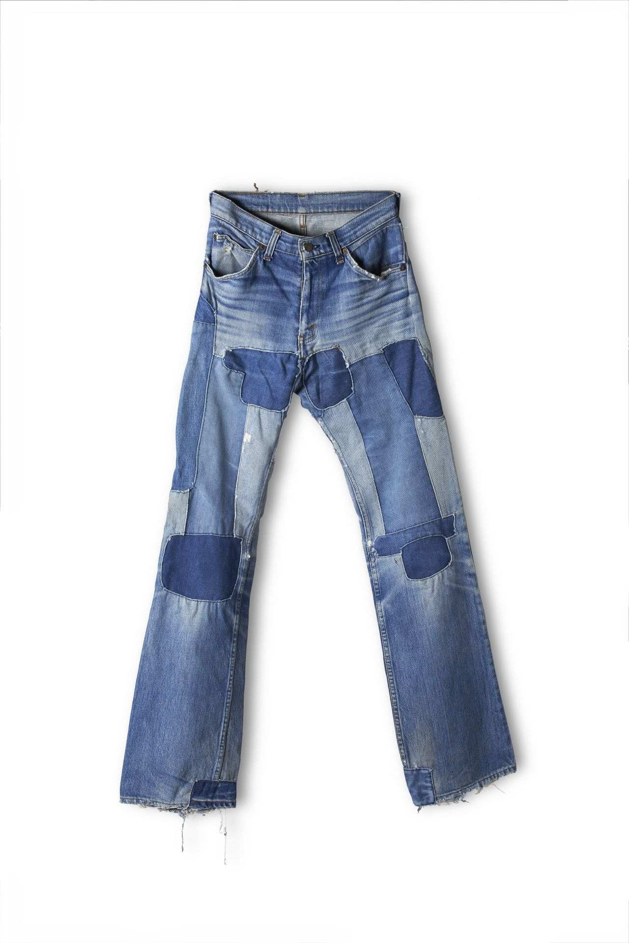 Blaue Jeanshose mit 5 Taschen, viele auf- und eingenähte Jeansflecken in unterschiedlichen Blautönen im Bereich der Oberschenkel, Knie und des Saums.