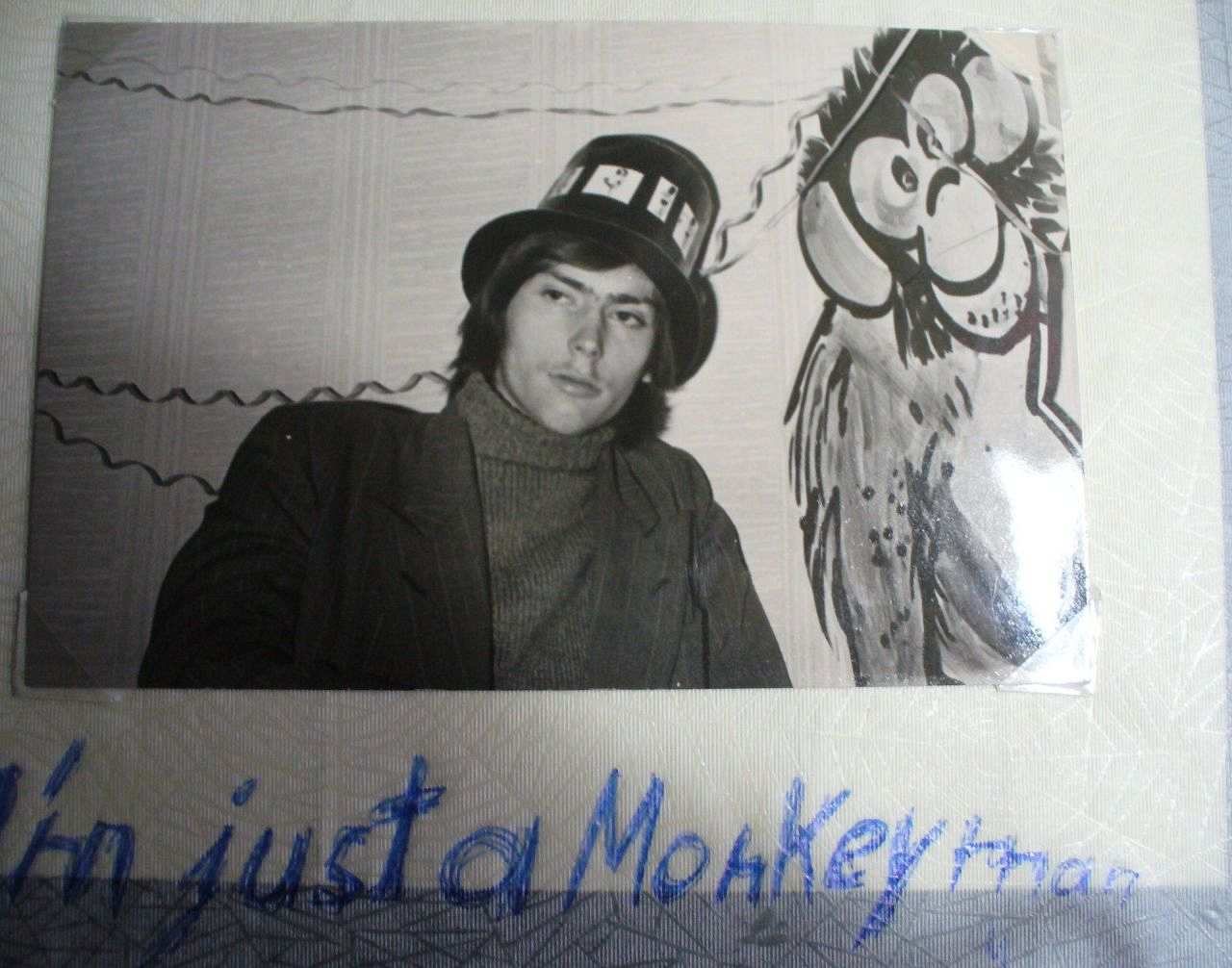 Ein junger Mann mit Hut und längeren Haaren ist vor dem Hintergrund eines gemalten Affen zu sehen. Unter das Foto ist 