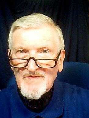 Farbige Fotografie, Porträtbild von Alfred Keffel mit ca. 73 Jahren: weiße Haare mit Seitenscheitel, braune Hornbrille, weißer Bart. Keffel sitzt auf einem blauen Bürostuhl, im Hintergrund ist ein dunkler Vorhang zu sehen. Das Foto hat er mit einer Webcam selbst geschossen.