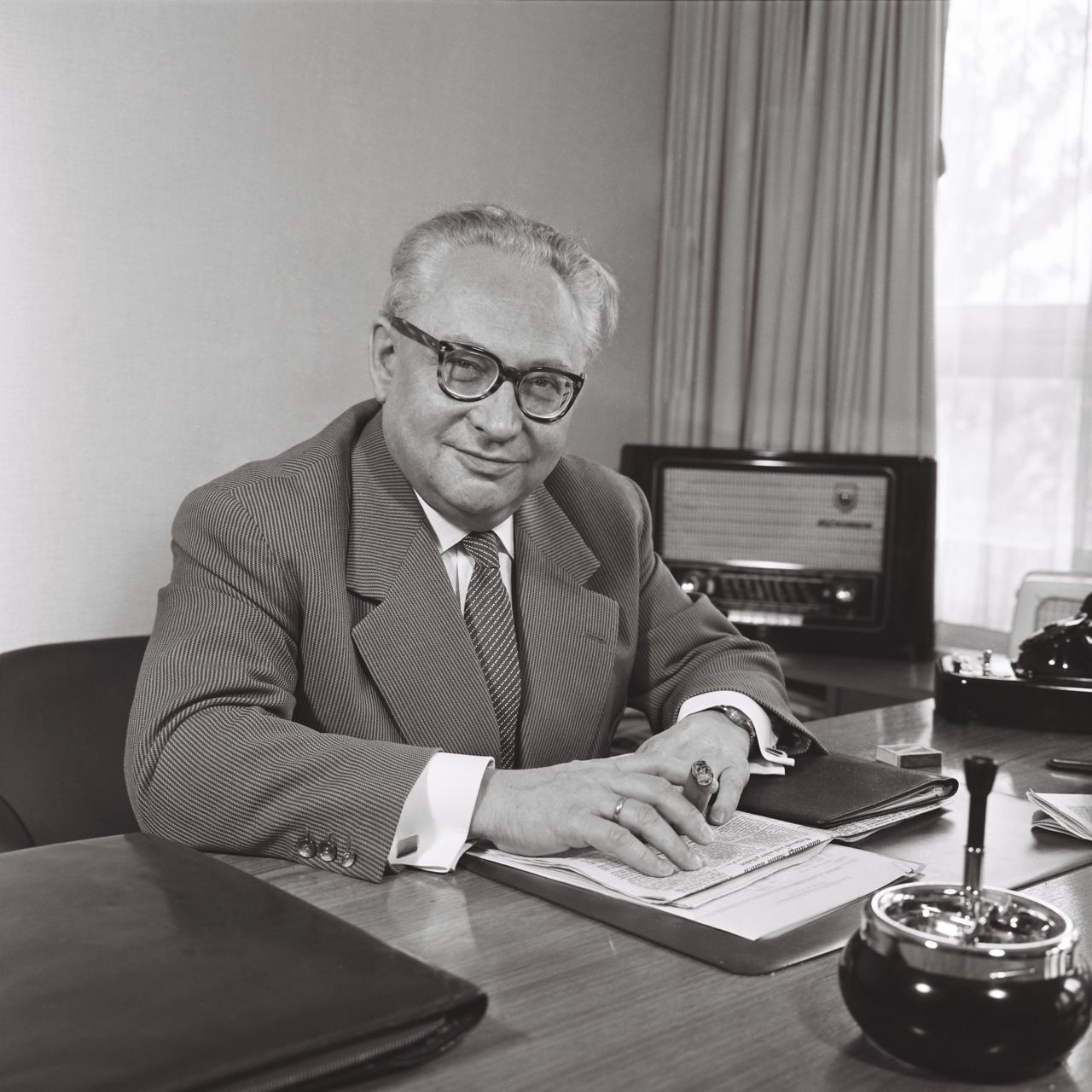 Erich Ollenhauer, Vorsitzender der SPD, am Schreibtisch in seinem Büro (mit Zigarre und Radiogerät i.H.), 1957.