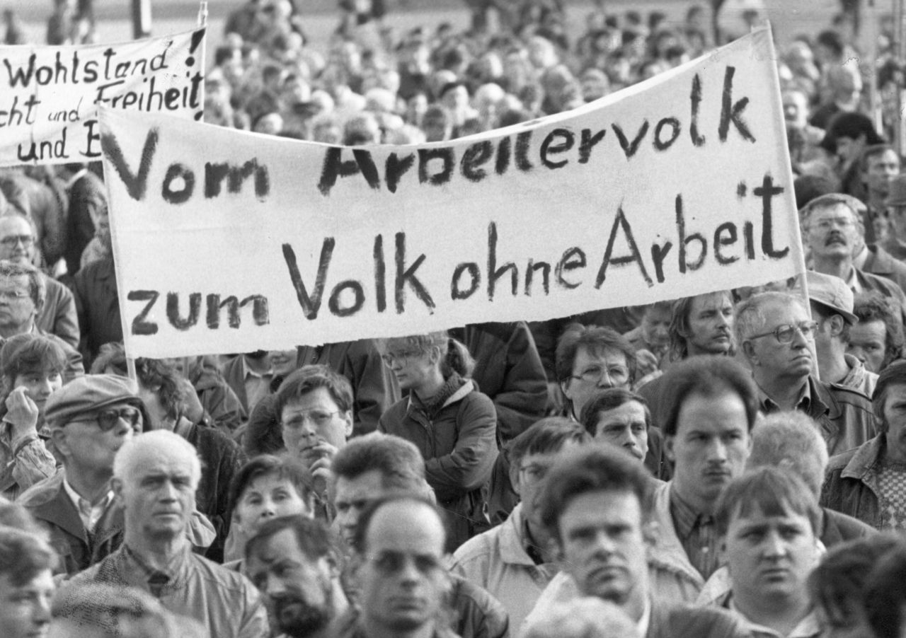 schwarzweiß Fotografie, Detailaufnahme einer großen Menschenmenge während einer Montagsdemonstration in Leipzig. Zentral im Bild ist ein großes Transparent mit der Aufschrift: Vom Arbeitervolk zum Volk ohne Arbeit. 