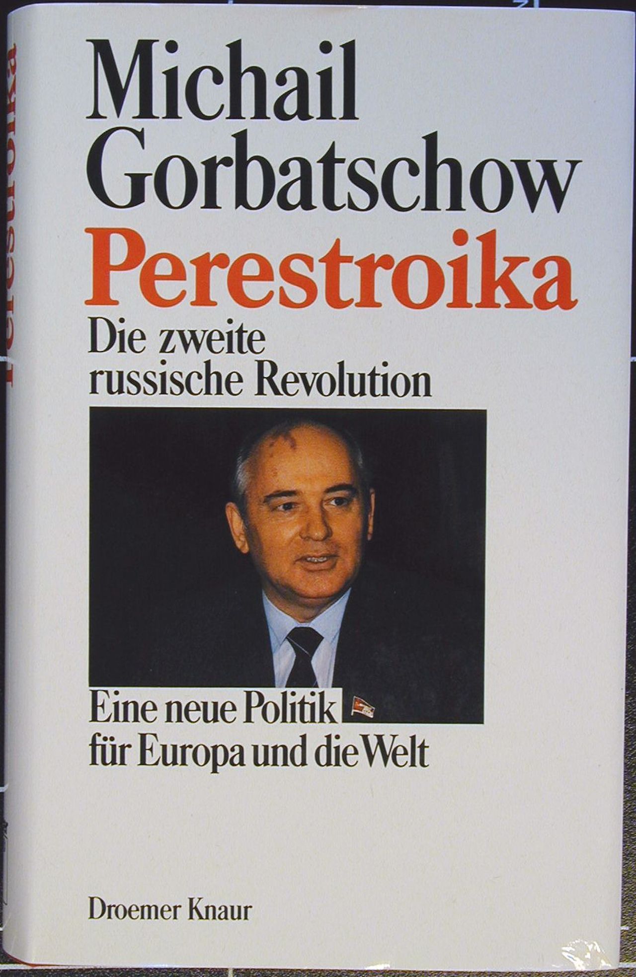 Rotes Buch; Rückenbeschriftung schwarz: Autor und Titel; Schutzumschlag weiß; Vorderseite: Farbporträt Gorbatschows; Text (schwarz, rot): Michail Gorbatschow, Perestroika, Die zweite russische Revolution, Eine neue Politik für Europa und die Welt. Darunter Angabe des Verlags: Droemer Knaur.