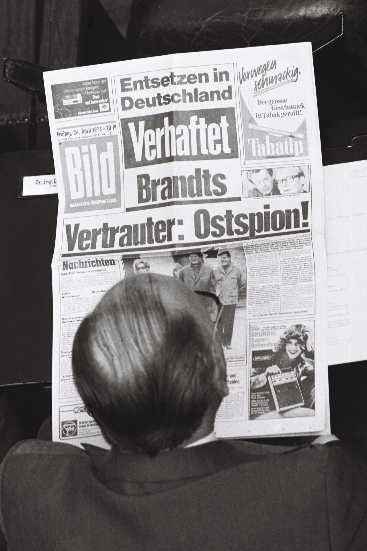 Schwarz-weiß-Foto. Kopf und Schulterbereich eines Bundestags-Abgeordneten von oben aufgenommen. Er liest die Bild-Zeitung mit der Titelschlagzeile: 