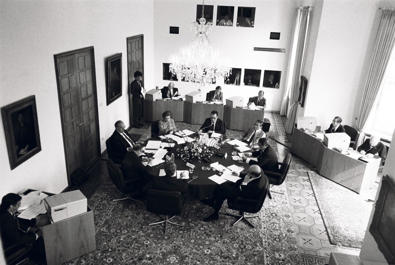 Schwarzweiß-Foto von oben; die Staats- und Regierungschefs sitzen an einem runden Konferenztisch im Kabinettssaal des Palais Schaumburg; darauf mittig ein Blumenbouquet, Mikrofone und Schriftstücke. Etwas entfernt vom Tisch einige Dolmetscher-Arbeitsplätze.
