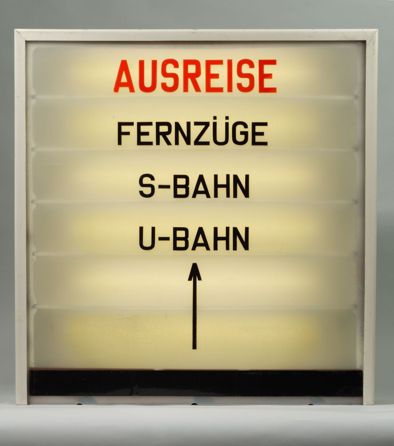 Trübes Kunststoffschild mit rot-schwarzem Text: Ausreise / Fernzüge / S-Bahn / U-Bahn. Darunter Pfeil nach oben.
