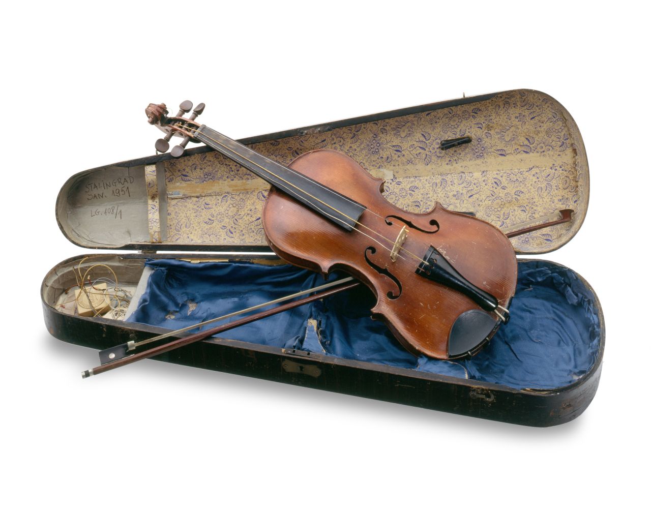 Der Korpus der Geige sowie die Schnecke sind aus rötlich-braunem Holz gefertigt. Hals und Saitenhalter sind schwarz. Die Geige liegt auf einem blauen Seidentuch in einem Geigenkasten, dessen Deckel beige ausgeschlagen ist. Im Deckel klemmt der Bogen.