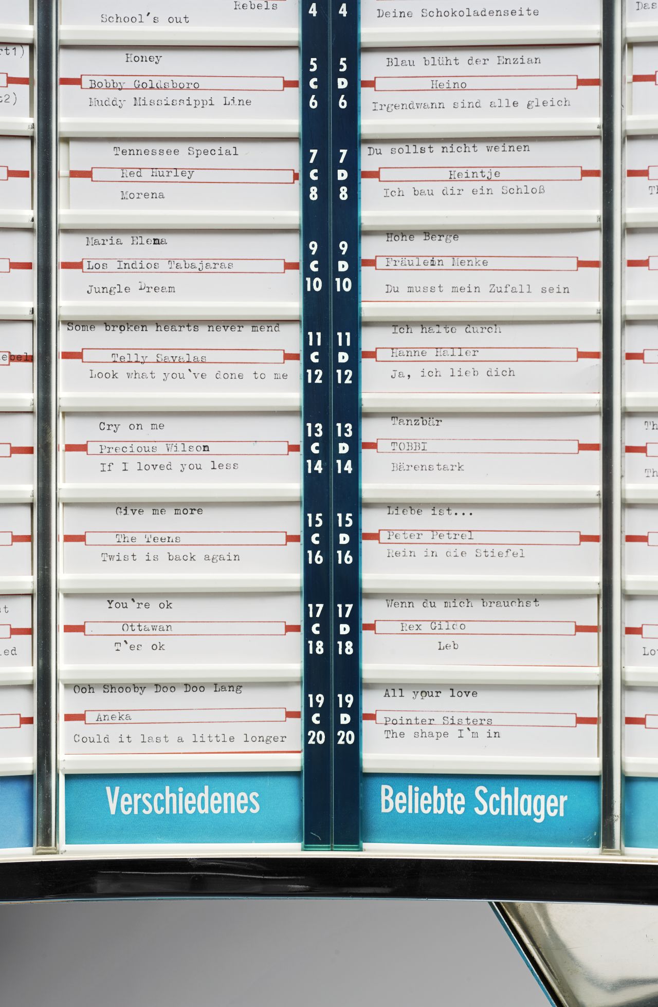 Im unteren Teil gitterförmige, goldfarbene Lautsprecherabdeckung mit aufgelegtem Stern; darüber Schriftzug: Continental; darüber Wählscheibe.
Oberer Teil außen grau, im Inneren vorwiegend hellgrün; unter einer Glaskuppel Plattenteller; darüber großes gebogenes Teil mit kleinen Schildern für die Musik-Titel (nur teilweise beschriftet); Geldeinwurf vorne rechts; ganz oben Mitte: Schloss. Rechts: Stromkabel.
Rückseite Etikett mit Herstellerangabe und technischen Daten (220 Volt, 230 Watt, Serien-Nummer 13418).
