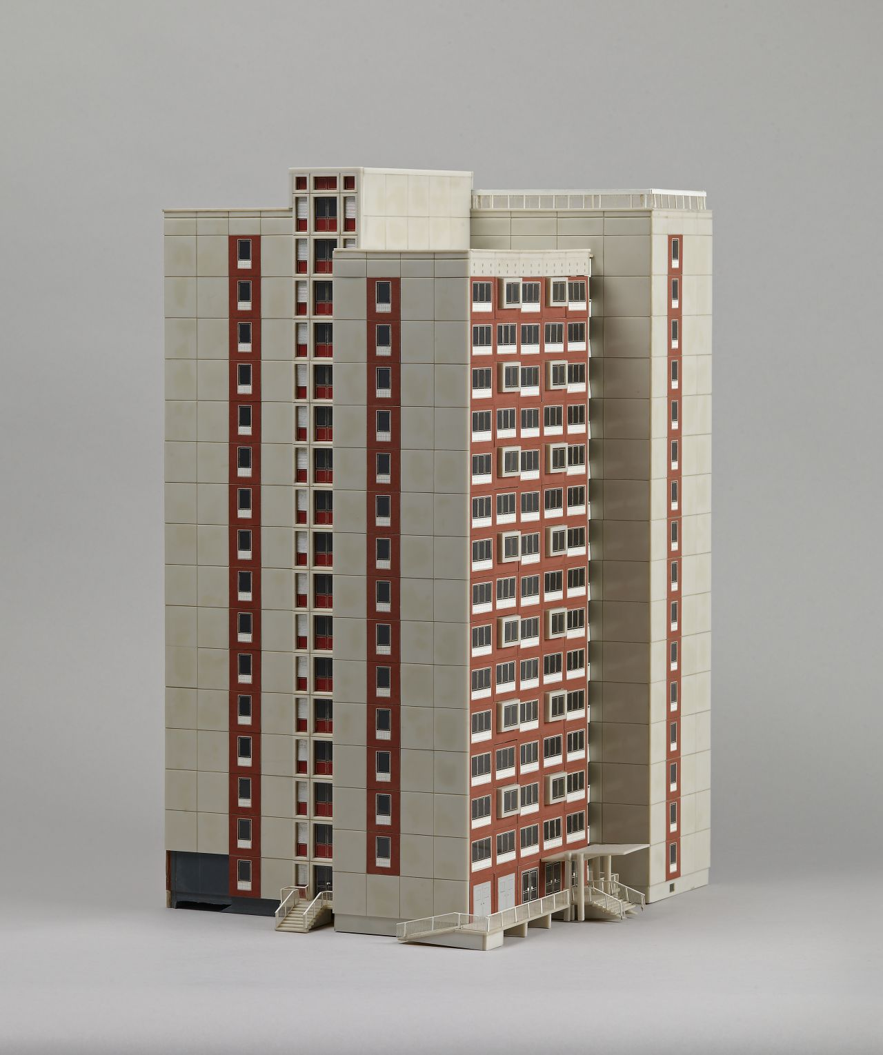 Modell: Rot-beigefarbenes Hochhaus aus 4 Einzeltürmen mit unterschiedlicher Höhe zusammengefügt. Zwei Treppenaufgänge außen. 
