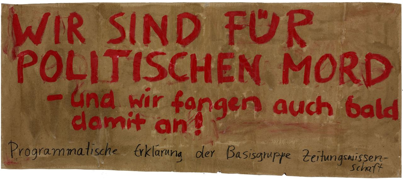 Braunes Transparent aus Papier mit roten handschriftlichen Großbuchstaben: Wir sind für politischen Mord - und wir fangen auch bald damit an!, darunter in schwarz: Programmatische Erklärung der Basisgruppe Zeitungswissenschaften.